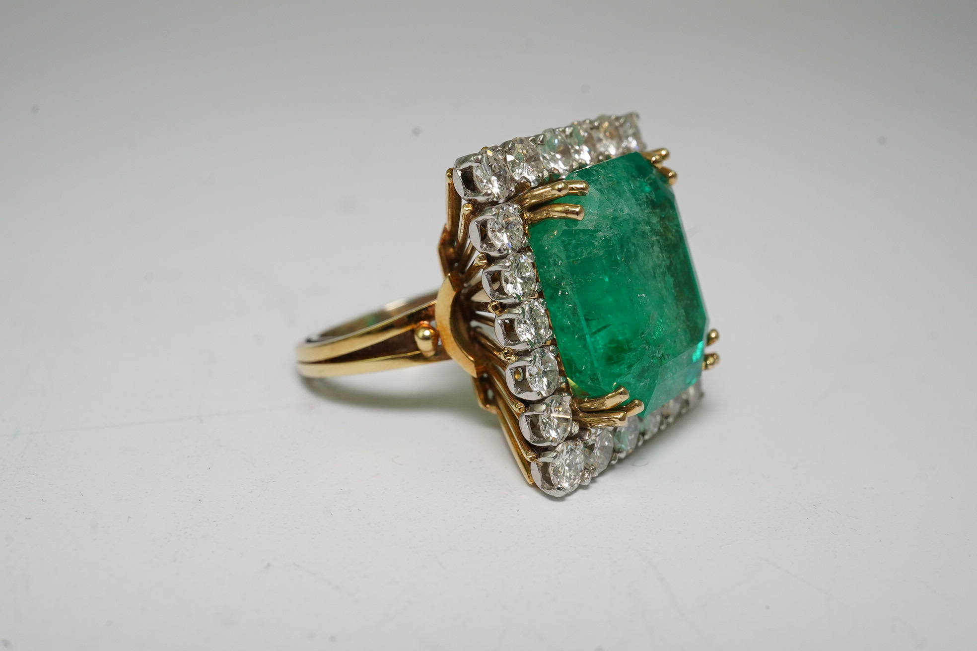 A Stern 18ct white and yellow gold, emerald and diamond dress ring, the central green emerald cut emerald approximately 8.0ct and surrounded by twenty two circular cut diamonds, approximately 2.7ct total